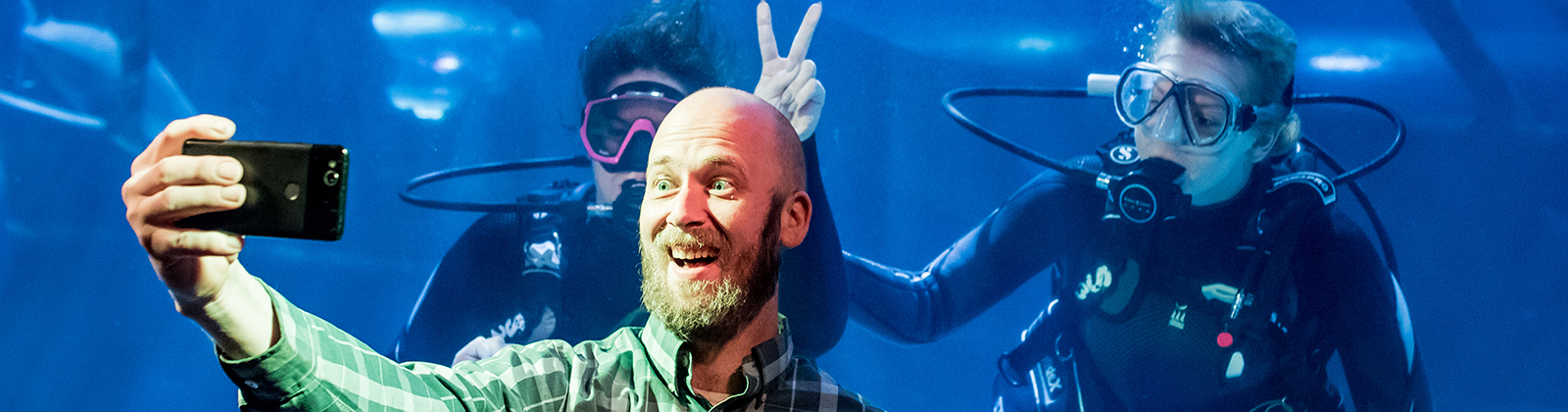 A man taking a selfie in front of two divers underwater,.